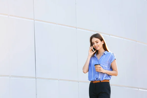 Jovem empresária com xícara de café saboroso falando por telefone celular ao ar livre — Fotografia de Stock