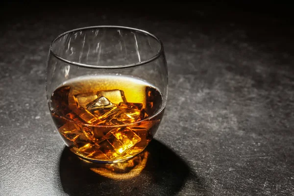 Glass of cold whiskey with ice on dark table — Stock Photo, Image