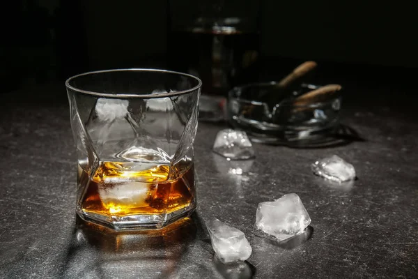 Glass of cold whiskey with ice on dark table — Stock Photo, Image