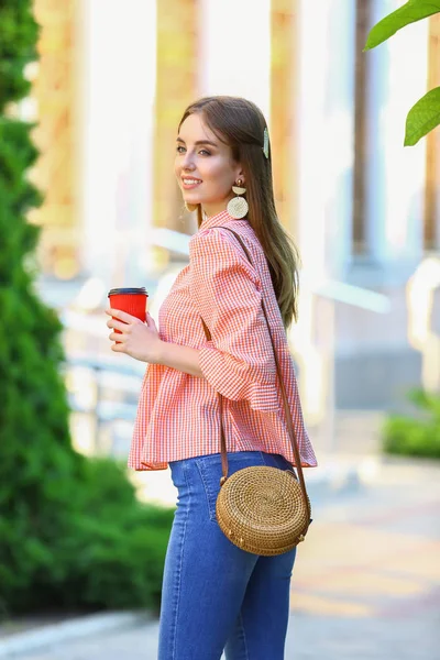 Stylish young woman with cup of coffee outdoors — Stock Photo, Image