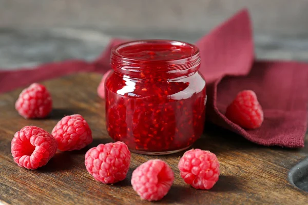 Tasty raspberry jam in jar with berries on wooden board — Stock Photo, Image