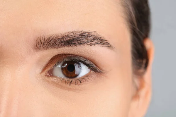 Ung kvinna med vackra ögonbryn på grå bakgrund, närbild — Stockfoto