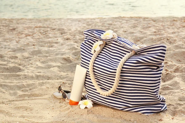 Bag with sunscreen cream and sunglasses on sand beach — Stock Photo, Image