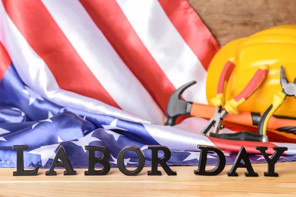 Bandera de EE.UU., hardhat, herramientas y texto LABOR DAY sobre mesa de madera — Foto de Stock