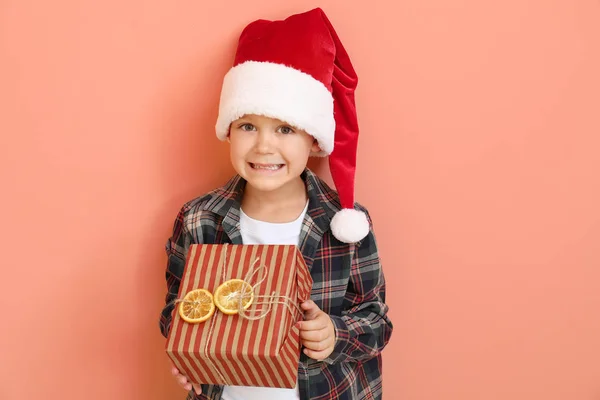 Little boy in Santa hat and with Christmas gift on color background — Stock Photo, Image