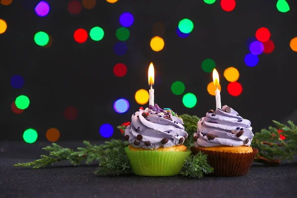 Tasty festive cupcakes and fir branch on table against defocused lights — Stock Photo, Image