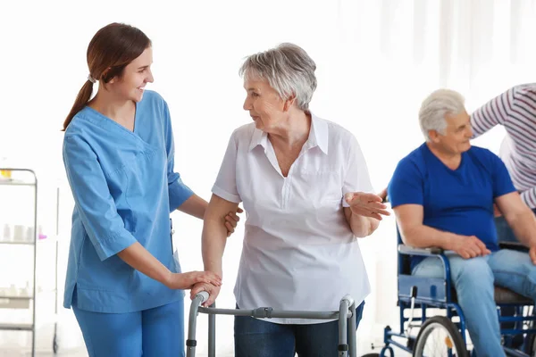Young caregiver looking after disabled senior woman in nursing home — Stock Photo, Image