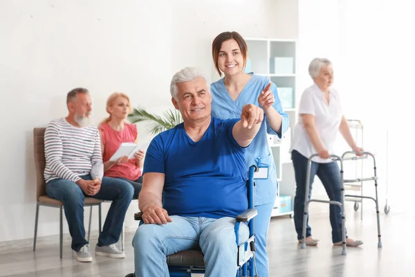 Young caregiver looking after disabled mature man in nursing home — Stock Photo, Image