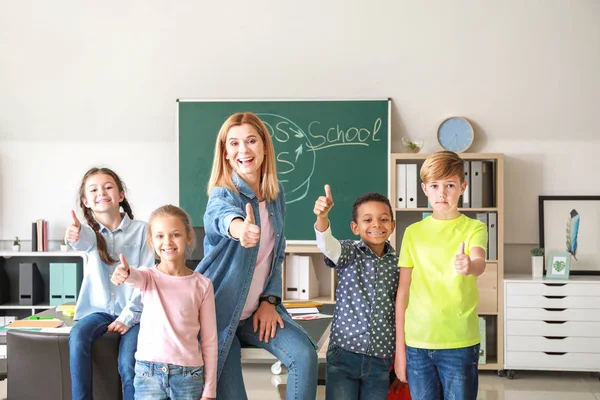 Śliczne dzieci z nauczycielem pokazując kciuk w górę gest w klasie — Zdjęcie stockowe