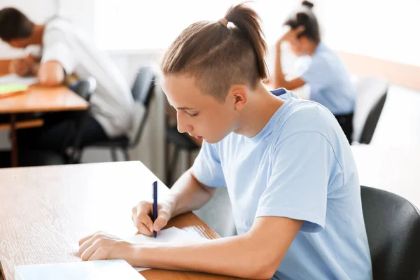 Tiener jongen passeren school test in klaslokaal — Stockfoto