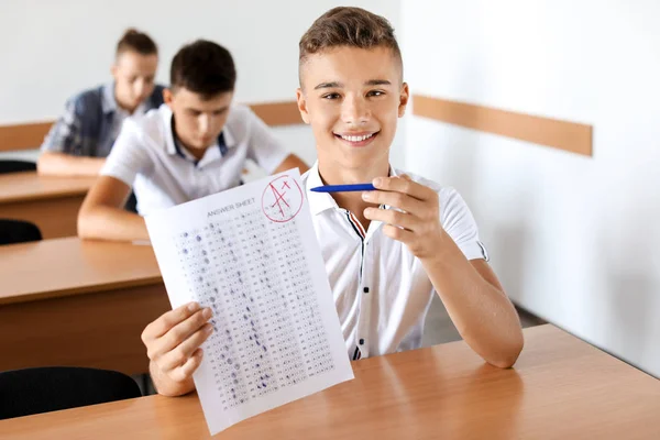 Happy boy with results of school test in classroom