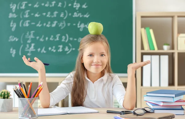 Девочка с яблоком сидит за столом в классе — стоковое фото