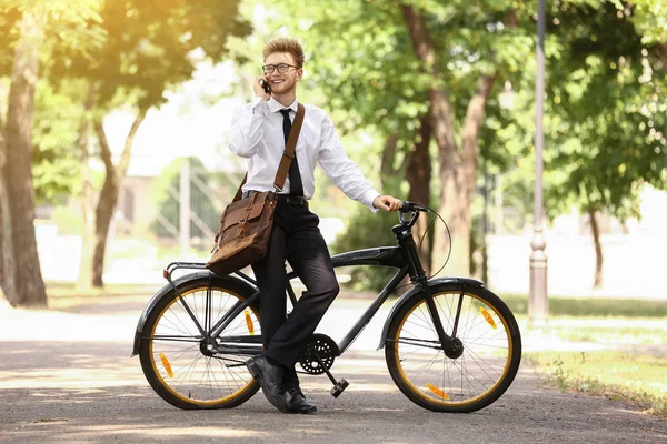 Joven hombre de negocios con bicicleta hablando por teléfono al aire libre — Foto de Stock