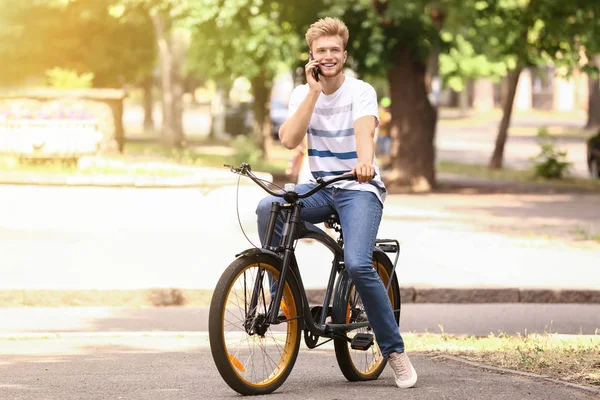 Νέος άνθρωπος μιλάει τηλεφωνικώς, ενώ ιππασία ποδήλατο σε εξωτερικούς χώρους — Φωτογραφία Αρχείου