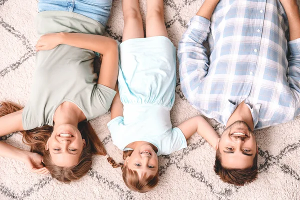 Portrait of happy young family lying on carpet at home — Stock Photo, Image