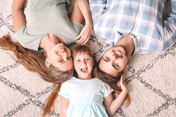 Portrait of happy young family lying on carpet at home — Stock Photo, Image