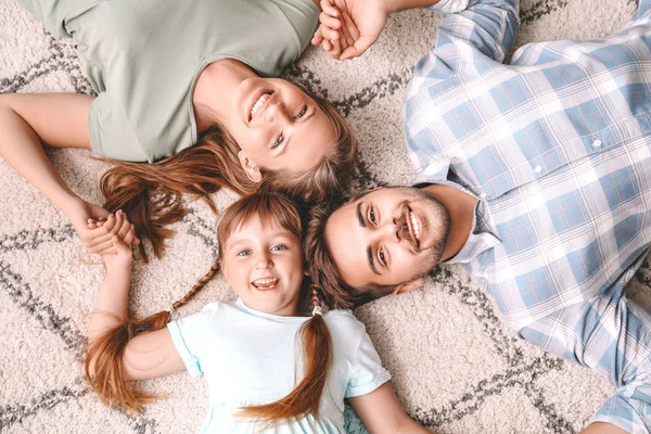 Retrato de família jovem feliz deitado no tapete em casa — Fotografia de Stock