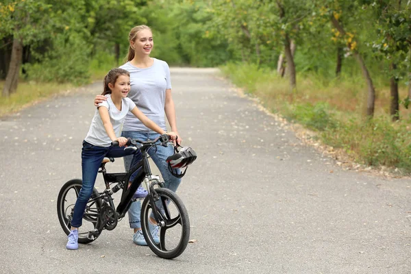 Mother teaching her daughter to ride bicycle outdoors — Stock Photo, Image