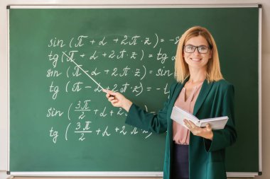 Sınıfta tahta yakın kitap ve işaretçi ile güzel matematik öğretmeni