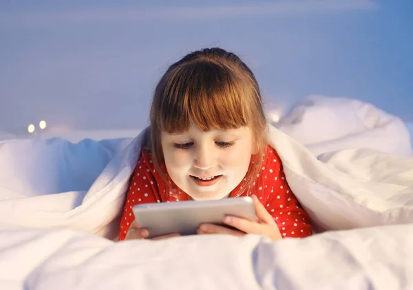 Schattig klein meisje met behulp van Tablet PC in bed 's nachts — Stockfoto