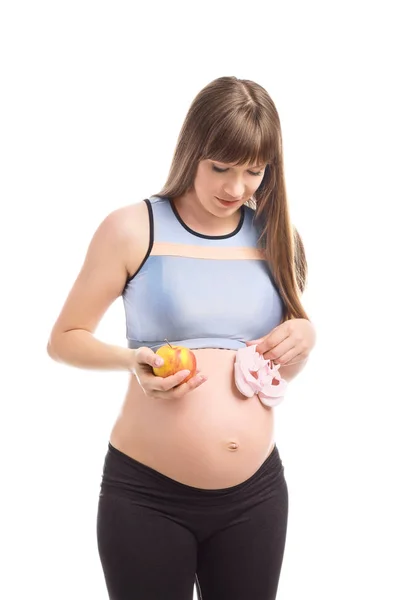 Beautiful pregnant woman with apple and baby booties on white background — Stock Photo, Image