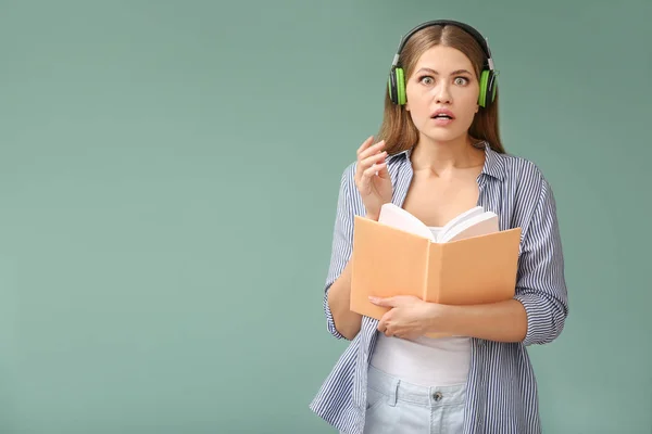 Shocked young woman listening to audiobook on color background — Stock Photo, Image