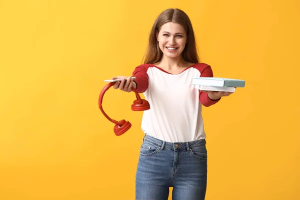 Junge Frau mit Büchern, Handy und Kopfhörern auf farbigem Hintergrund. Konzept der Wahl zwischen Lesen und Hören — Stockfoto