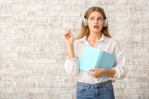 Mujer joven reflexiva escuchando audiolibro contra la pared de ladrillo —  Fotos de Stock