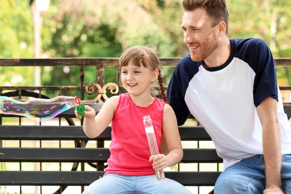 Glücklicher Vater und seine kleine Tochter beim Blasen von Seifenblasen im Freien — Stockfoto