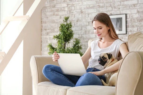 Молодая женщина с симпатичной собакой-мопсом, работающей на ноутбуке дома — стоковое фото