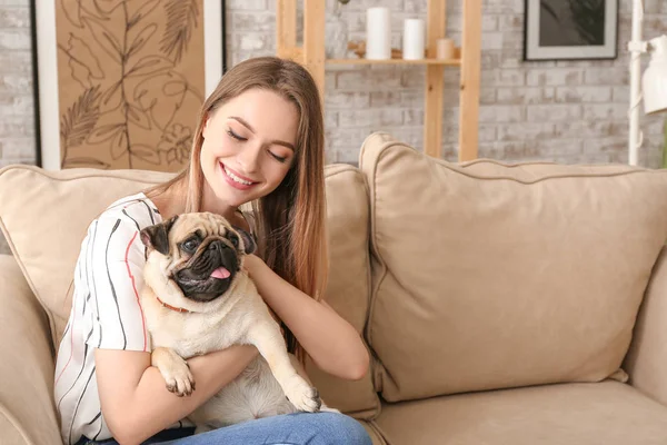 Beautiful young woman with cute pug dog sitting on sofa at home — Stock Photo, Image