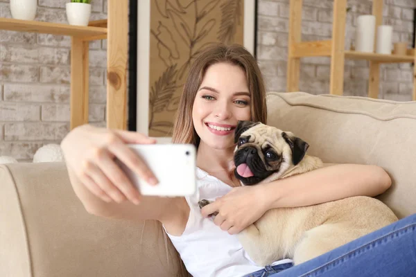 Beautiful young woman with cute pug dog taking selfie at home — Stock Photo, Image