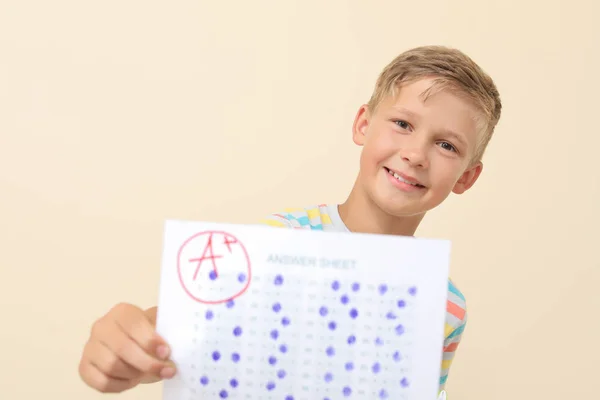 Menino feliz com folha de resposta para teste escolar em fundo claro — Fotografia de Stock