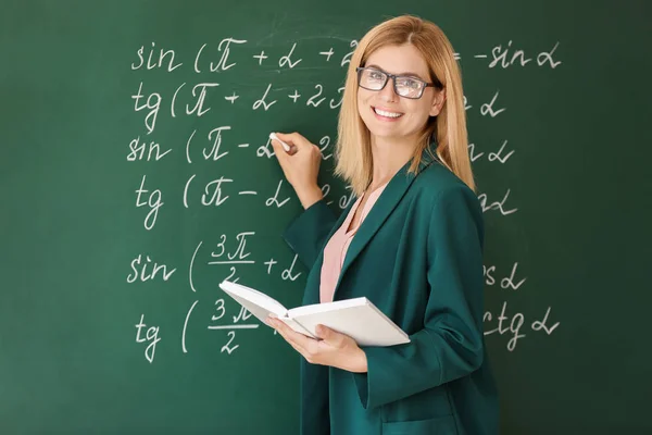 Hermoso profesor de matemáticas con libro cerca de pizarra en el aula — Foto de Stock