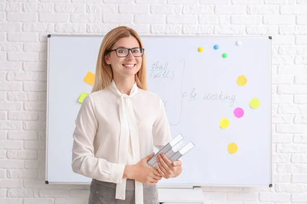 Beautiful English teacher with books in classroom