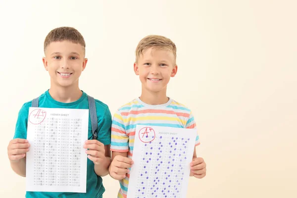 Meninos felizes com folhas de resposta para teste escolar em fundo claro — Fotografia de Stock