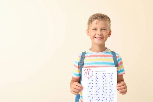Ragazzo felice con foglio di risposta per test scolastici su sfondo chiaro — Foto Stock