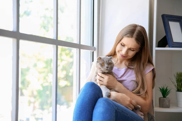 Beautiful woman with cute cat sitting near window — Stock Photo, Image