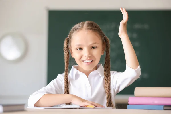 Милая маленькая девочка поднимает руку во время урока в классе — стоковое фото