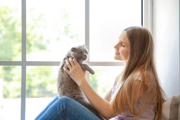 Beautiful woman with cute cat sitting near window — Stock Photo, Image