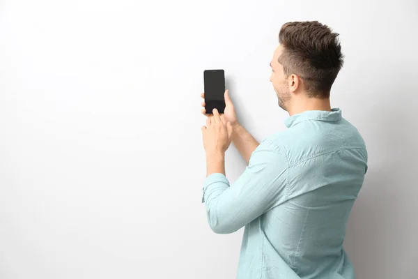 Young man with modern mobile phone near wall — Stock Photo, Image