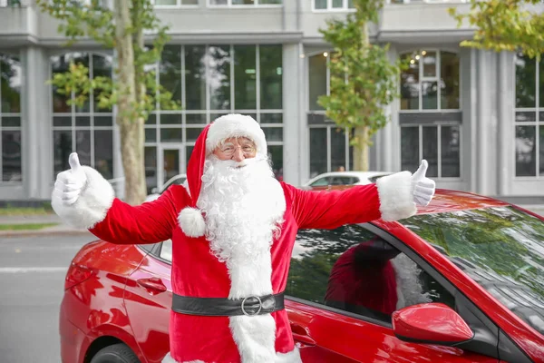 Papai Noel mostrando gesto de polegar para cima perto do carro ao ar livre — Fotografia de Stock