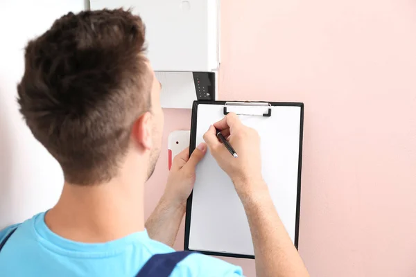Electrician with clipboard checking alarm system indoors — Stock Photo, Image