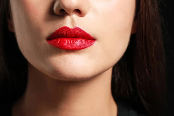 Bella giovane donna con rossetto luminoso su sfondo scuro, primo piano — Foto Stock