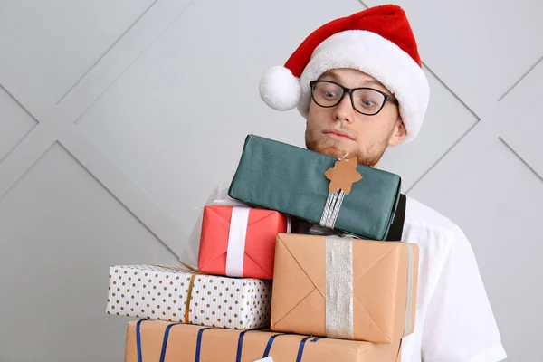 Young man with many Christmas gift boxes on light background — Stock Photo, Image