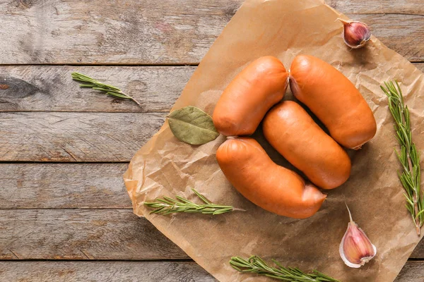 Parchment with tasty sausages on wooden table — Stock Photo, Image