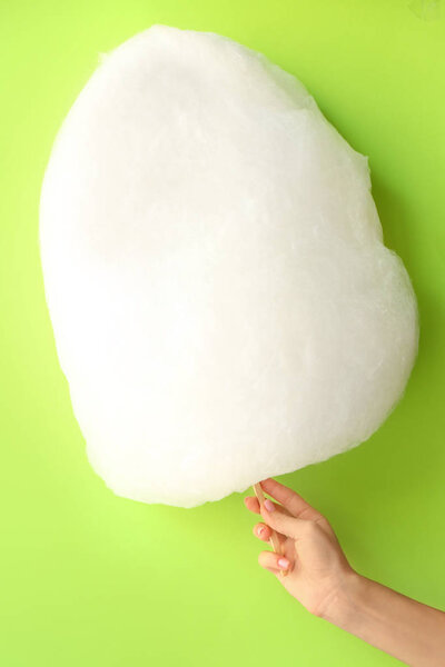 Женская рука с вкусной сладкой ватой на цветном фоне
