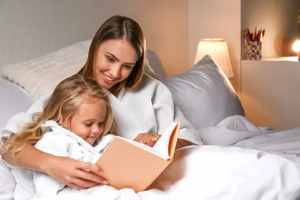 Happy woman with her little daughter reading book in bed — Stock Photo, Image