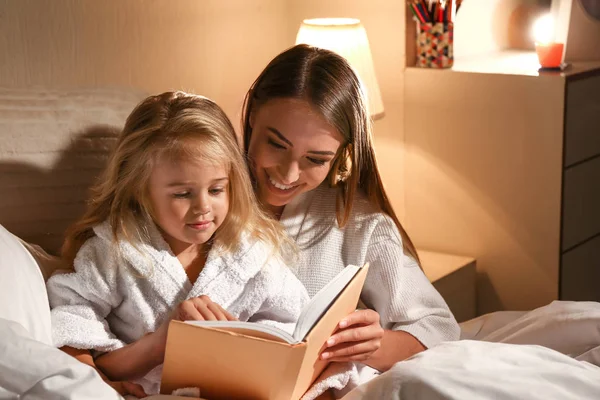 Happy woman with her little daughter reading book in bed — Stock Photo, Image