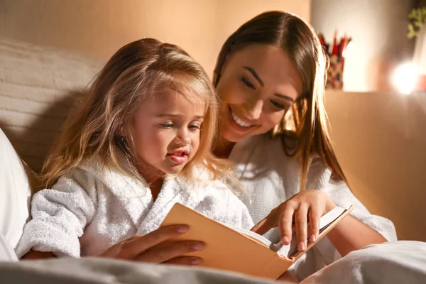 Happy woman with her little daughter reading book in bed — Stock Photo, Image